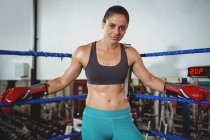 Confident female boxer leaning on boxing ring in fitness studio — Stock Photo