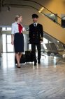 Pilote et hôtesse de l'air marchant avec leurs sacs trolley dans le terminal de l'aéroport — Photo de stock