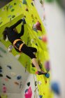 Mujer practicando escalada en roca en muro de escalada artificial en gimnasio - foto de stock