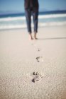 Gros plan sur les empreintes de pas et la partie basse d'une femme marchant sur la plage — Photo de stock
