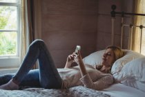 Beautiful woman lying on bed and using mobile phone in bedroom at home — Stock Photo