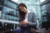 Бізнес-леді сидить біля фонтану і використовує мобільний телефон за межами офісної будівлі — стокове фото