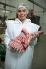 Retrato de una carnicera sosteniendo carne en una fábrica de carne - foto de stock