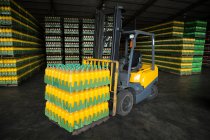 Empilement de bouteilles de jus emballées et chariot élévateur dans l'entrepôt — Photo de stock