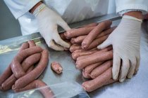 Mains de boucher emballant des saucisses crues dans une usine de viande — Photo de stock