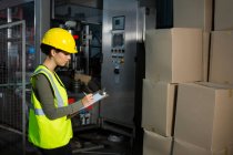 Side view of female worker writing on clipboard in warehouse — Stock Photo