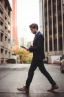 Uomo d'affari che utilizza tablet digitale mentre attraversa la strada urbana — Foto stock