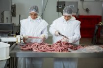Жіночі м'ясники, що ріжуть ковбаски на м'ясному заводі — стокове фото