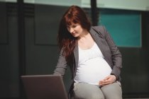 Femme d'affaires enceinte utilisant un ordinateur portable dans les locaux du bureau — Photo de stock