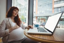 Embarazada mujer de negocios usando laptop en oficina cafetería - foto de stock