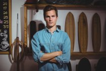 Confident man standing with arms crossed in surfboard shop — Stock Photo