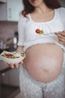 Mulher grávida tendo salada na cozinha em casa — Fotografia de Stock