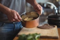 Primo piano di mani di uomo che tiene fette di patate in pentola di stufato in cucina — Foto stock