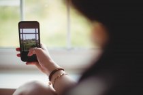 Вид сзади женщины, делающей фото на мобильном телефоне из окна — стоковое фото
