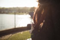 Крупный план женщины с помощью мобильного телефона во время хранения цифровой камеры — стоковое фото