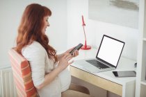 Pregnant woman using mobile phone in study room at home — Stock Photo