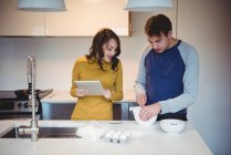 Couple using digital tablet while preparing cookies in kitchen at home — Stock Photo