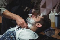 Cliente afeitándose la barba con afeitadora en la peluquería - foto de stock
