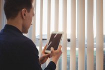 Geschäftsmann nutzt digitales Tablet in der Nähe von Jalousien im Büro — Stockfoto