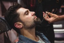 Мужчина, обрезающий бороду ножницами в парикмахерской — стоковое фото