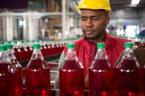 Trabalhador masculino grave monitorando garrafas de suco vermelho na fábrica — Fotografia de Stock