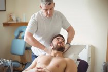 Fisioterapeuta examinando cuello de paciente masculino en clínica - foto de stock
