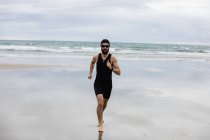 Homem em traje de natação e touca de natação correndo na praia — Fotografia de Stock