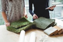 Dirigenti aziendali esaminando tappeto erboso artificiale durante l'utilizzo di tablet digitale in ufficio — Foto stock