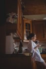 Schöne Frau benutzt Handy, während sie zu Hause in der Küche Kaffee trinkt — Stockfoto