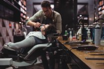 Varios trimmers en tocador con peluquero afeitado cliente en segundo plano en peluquería - foto de stock