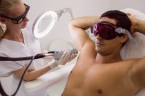 Doctor performing laser hair removal on male patient skin in clinic — Stock Photo