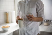 Середній розділ людини, що використовує мобільний телефон, маючи чашку кави вдома — стокове фото