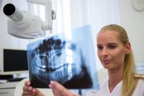 Dentista mirando la placa de rayos X dental en la clínica - foto de stock