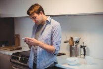 Homem usando telefone celular enquanto prepara café da manhã na cozinha em casa — Fotografia de Stock