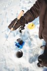 Mid section of ice fisherman holding fishing rod over ice hole — Stock Photo
