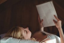 Mulher bonita deitada na cama e revista de leitura no quarto em casa — Fotografia de Stock