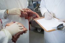 Mid section of butchers maintaining records on clipboard at meat factory — Stock Photo