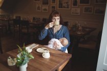 Mutter trinkt Kaffee, während sie ihre kleine Tochter im Café hält — Stockfoto