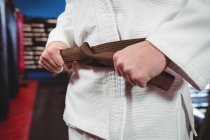 Mid section of karate player tying belt in fitness studio — Stock Photo