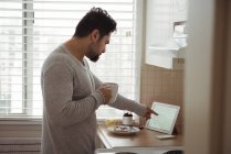 Homem usando tablet digital enquanto toma café na cozinha — Fotografia de Stock