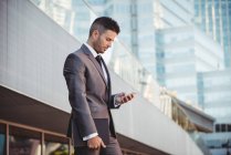 Бизнесмен, использующий мобильный телефон возле офисного здания — стоковое фото