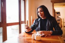 Красива жінка використовує мобільний телефон, маючи чашку кави в кафе — стокове фото