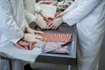 Mid section of butchers packing raw sausages at meat factory — Stock Photo