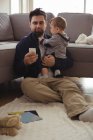 Father holding his baby while using mobile phone at home — Stock Photo
