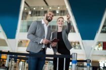 Businesswoman standing with her colleague and pointing at the distance at airport terminal — Stock Photo