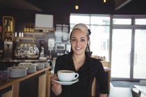Портрет официантки, стоящей с чашкой кофе в кафе — стоковое фото