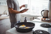 Чоловік використовує цифровий планшет під час приготування смажених яєць на кухні вдома — стокове фото