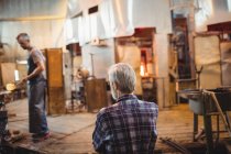 Glassblower looking at coworker working at glassblowing factory — Stock Photo