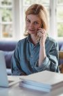 Красива жінка говорити на мобільний телефон, використовуючи ноутбук у вітальні на дому — стокове фото