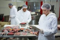 Female butcher maintaining records on clipboard at meat factory — Stock Photo